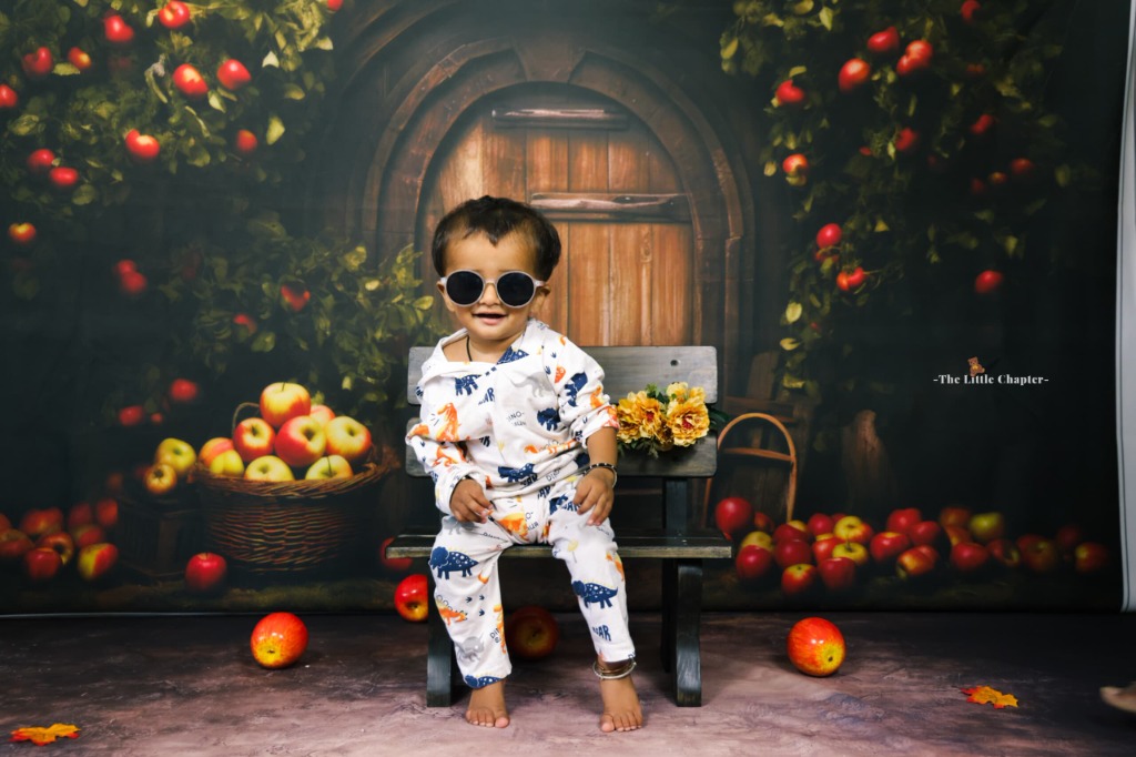 Baby wearing stylish sunglasses sitting on rustic wooden bench with apple harvest baskets