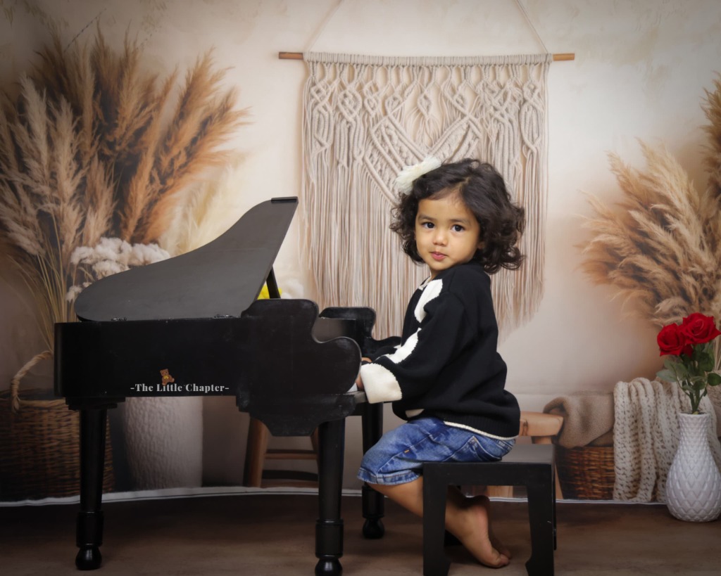 Little girl in black knit sweater playing miniature black grand piano with macrame backdrop
