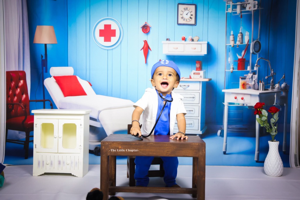 Laughing baby doctor in blue surgical cap and white lab coat seated at medical desk