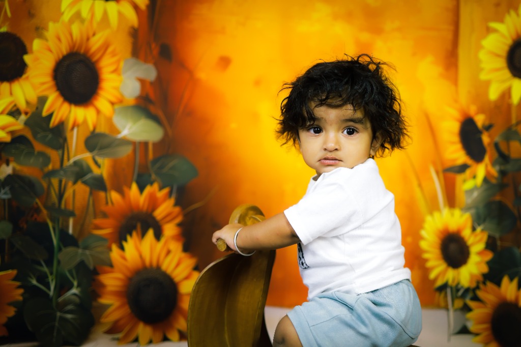 Curly-haired child on wooden rocking ride surrounded by blooming golden sunflowers