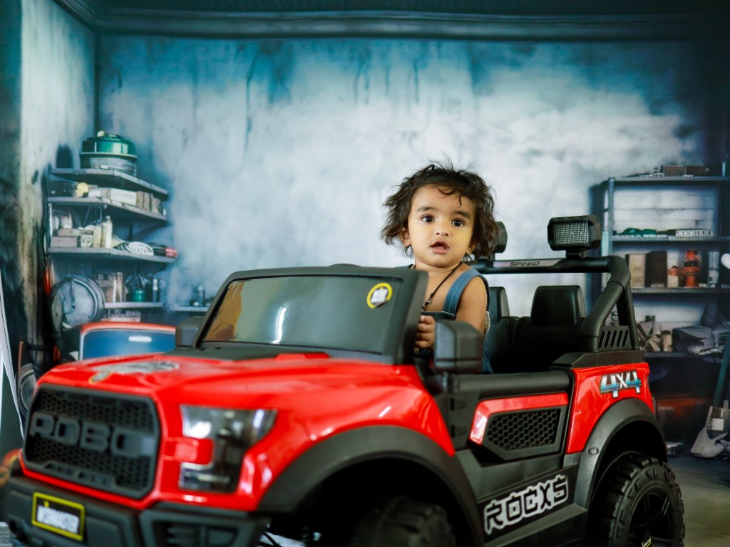Baby driving red off-road 4x4 electric Robo truck in auto repair garage set