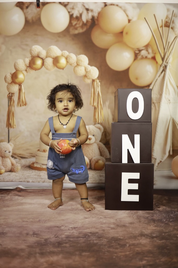 Baby standing proudly beside giant black 3D ONE letter blocks and teddy bear arch