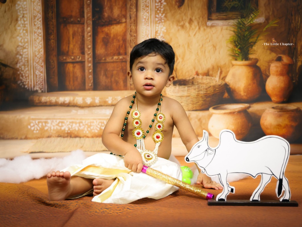 Baby boy in white traditional silk dhoti with gold borders sitting with white sacred calf figure