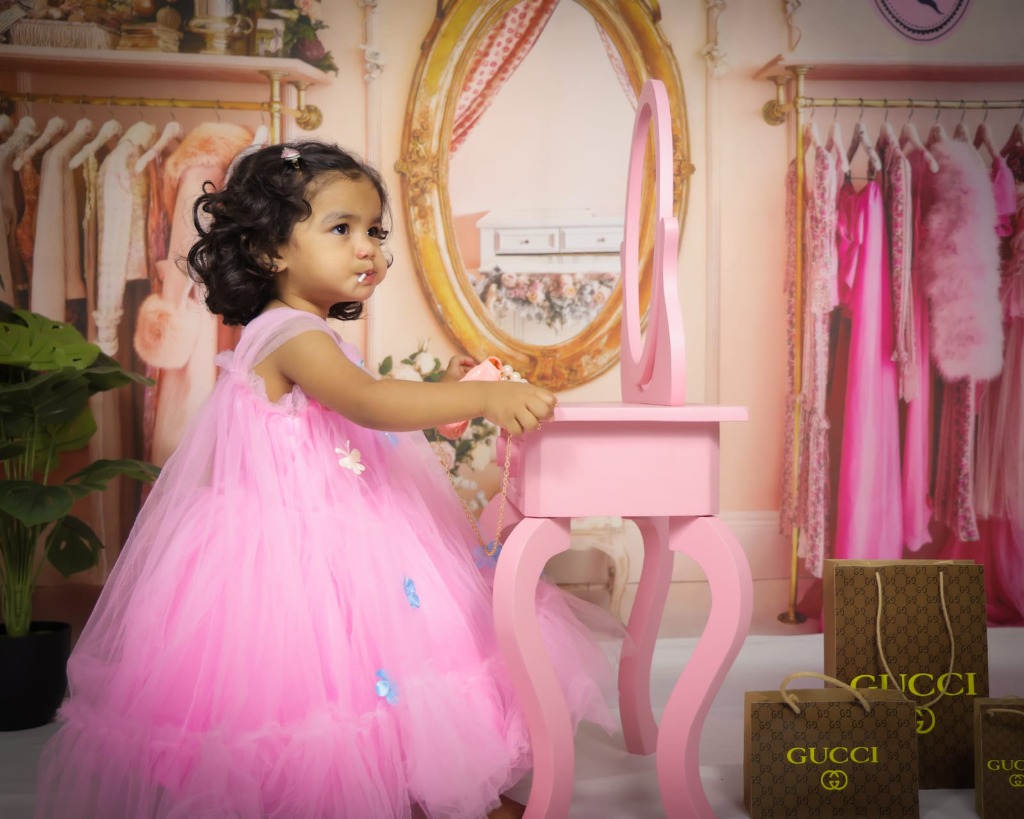 Little girl in pink ruffled tulle gown standing by pink mirror vanity table with Gucci gift bags